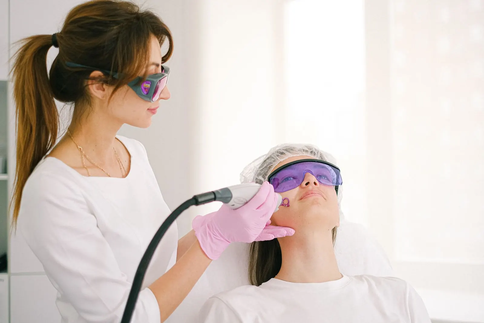 A practitioner performing a laser skin treatment on a patient wearing protective glasses